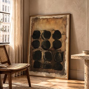 May include: A large rectangular framed wall art piece featuring a grid of twelve solid black circles painted on a textured, distressed background of earthy brown, tan, and cream tones, enclosed within a thin, simple metallic frame.