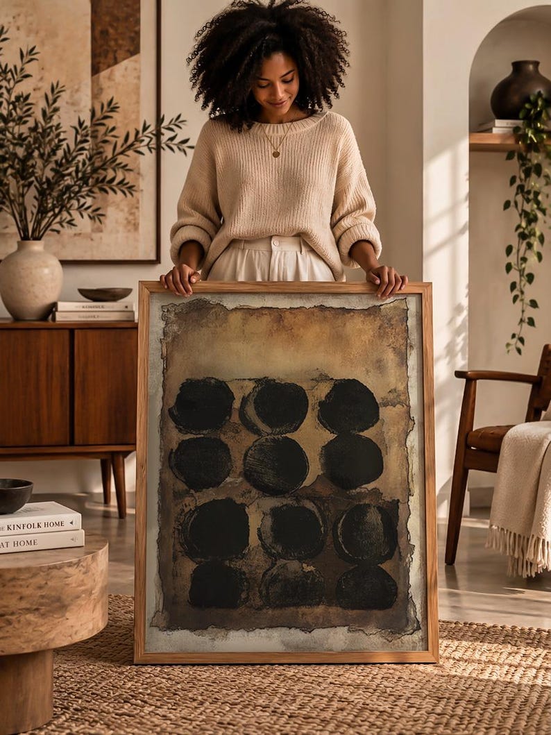 May include: A rectangular framed wall art piece featuring a textured, earthy brown background with a grid of nine solid black circles. The artwork is encased in a light-toned wooden frame with a visible grain, showcasing a distressed, aged paper aesthetic.