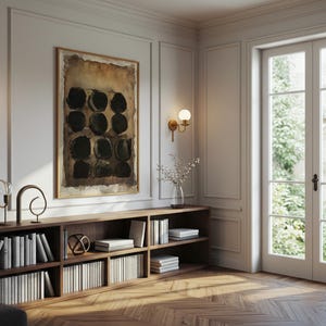May include: A low, rectangular wooden bookshelf with multiple compartments filled with white books, topped with decorative metal sculptures and a glass vase, positioned below a framed abstract painting with black circles on a brown background.