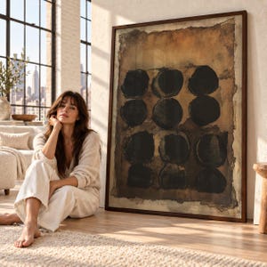 May include: A large rectangular framed wall art piece featuring a textured brown background with twelve dark black circles arranged in a grid pattern. The artwork has a distressed, uneven border and is encased in a dark brown wooden frame.