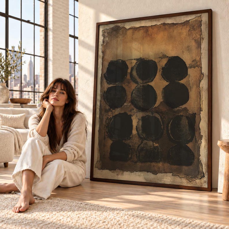 May include: A large rectangular framed wall art piece featuring a textured brown background with twelve dark black circles arranged in a grid pattern. The artwork has a distressed, uneven border and is encased in a dark brown wooden frame.