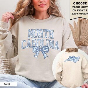 A woman wearing a beige sweatshirt with the text "NORTH CAROLINA" and a blue bow on the back.
