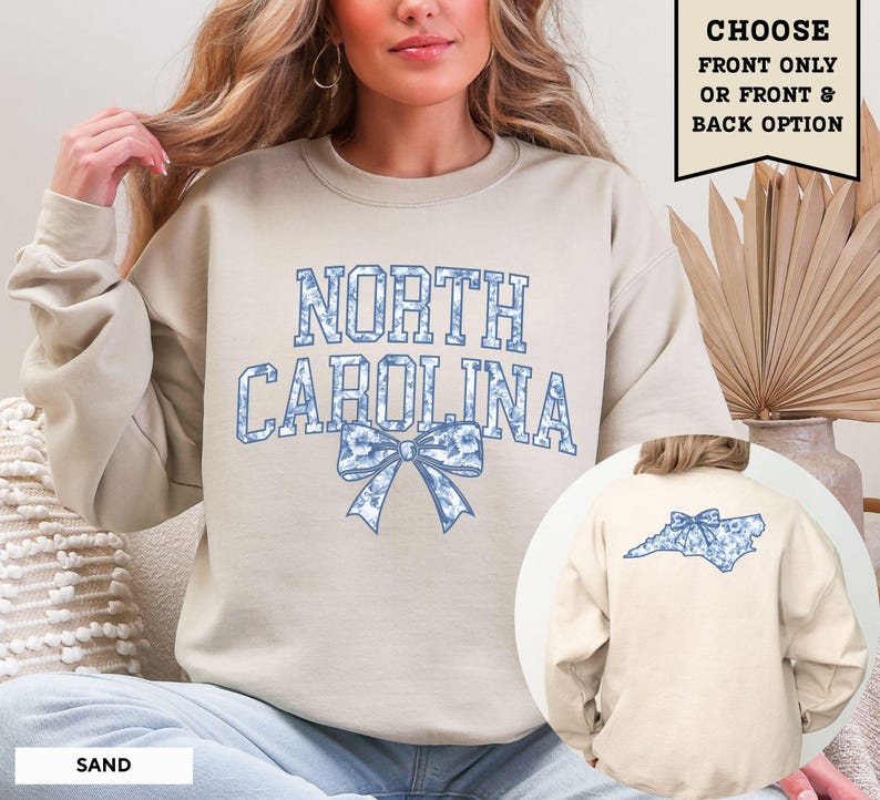 A woman wearing a beige sweatshirt with the text "NORTH CAROLINA" and a blue bow on the back.