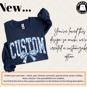 a navy blue sweatshirt with the word "CUSTOM" printed on it, along with a bow. The sweatshirt is displayed against a light background, and there is text next to it that reads "You've loved this design so much we've created a customizable option." The text also provides instructions for creating one's own text, such as name, year, Roman numerals, special word, career, hobby, team, mascot, and the possibilities are endless.