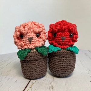May include: Two crocheted flower pot plushies, one pink and one red, with brown pots and green leaves.