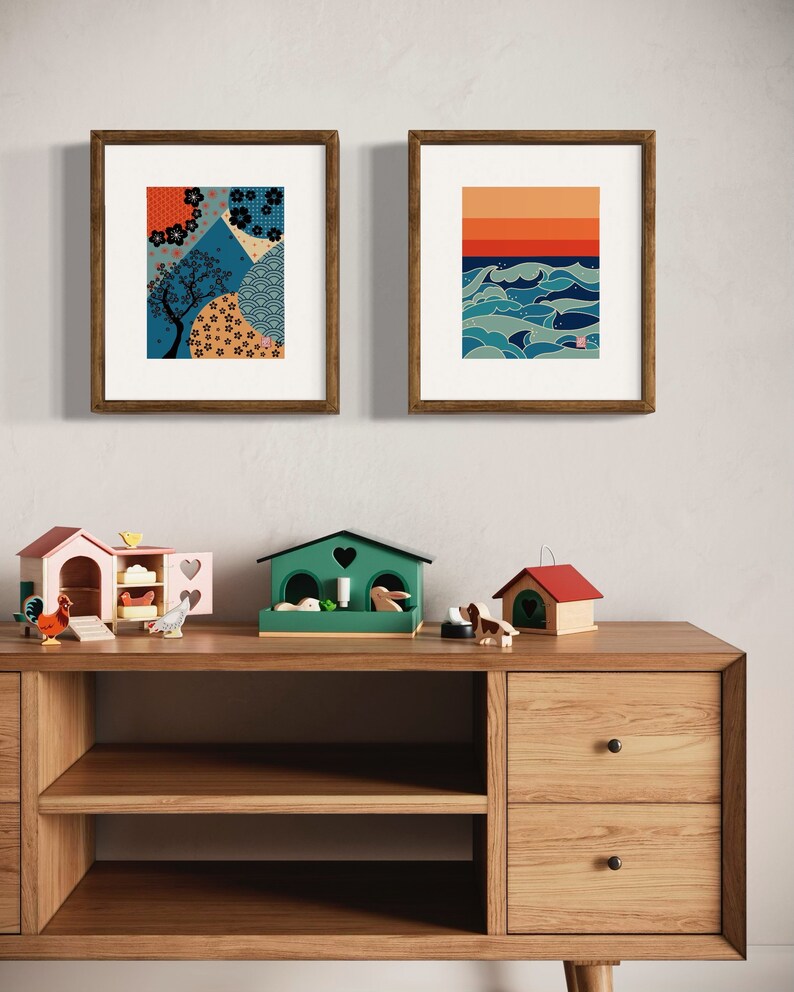 Puede incluir: Dos impresiones enmarcadas en una pared blanca, una con un dise&ntilde;o geom&eacute;trico azul y naranja y la otra con un dise&ntilde;o de olas azul y naranja. Debajo de las impresiones hay una estanter&iacute;a de madera con dos cajones y dos estantes. Hay tres casas de juguete de madera en la estanter&iacute;a.