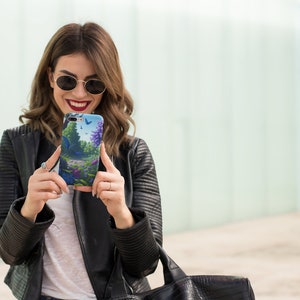 Könnte beinhalten: Eine Frau mit Sonnenbrille und einer schwarzen Lederjacke hält ein Smartphone mit einer bunten Handyhülle mit Blumen- und Schmetterlingsdesign.