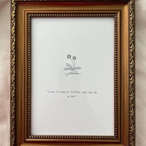 Puede incluir: Una impresión enmarcada con un marco dorado ornamentado. La impresión presenta un dibujo lineal simple de dos dientes de león y la cita: "incluso si eres pequeño, puedes hacer mucho."