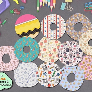 May include: A collection of circular adhesive overpatches featuring various school-themed patterns including pencils, apples, dinosaurs, and stationery items. Each patch has a central cutout. A green speech bubble states: NOTE: THESE ARE OVERPATCHES & SOLD INDIVIDUALLY.