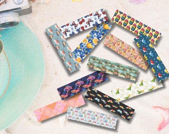 Peut inclure: Plusieurs autocollants rectangulaires décoratifs avec des motifs colorés. Les motifs incluent des nœuds, des citrons, des glaces, des requins et des moustaches. Les autocollants sont disposés sur une surface sablonneuse, sur le thème de l'été.