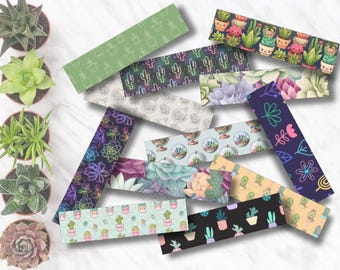 Peut inclure: Un assortiment de marque-pages colorés avec divers motifs de succulentes et de cactus. Les marque-pages présentent des motifs de plantes en pot, de cactus et d'arrangements floraux dans des tons de vert, de violet et de rose. Plusieurs succulentes en pot sont disposées autour des marque-pages.