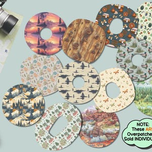 May include: A collection of circular adhesive overpatches featuring various printed designs including forest landscapes, wood grain, camping motifs, insects, ducks, and mountain scenes. A green speech bubble contains the text: NOTE: These ARE Overpatches & Sold INDIVIDUALLY.