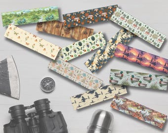 Peut inclure: Une collection de marque-pages rectangulaires présentant divers motifs sur le thème de la nature, notamment des forêts, des champignons, des insectes, des canards et des paysages, disposés avec une boussole, des jumelles noires et un thermos en métal.