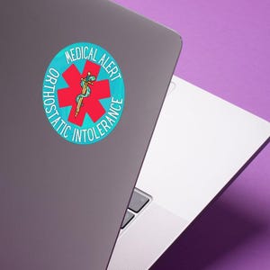 May include: A round sticker with the words "MEDICAL ALERT" and "ORTHOSTATIC INTOLERANCE" encircling a red cross with a medical symbol. The sticker is affixed to a gray laptop on a purple background.