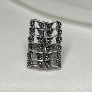 May include: A silver ring with a geometric design featuring a repeating pattern of small black stones.