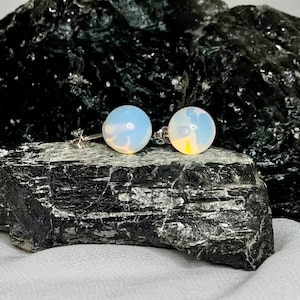 May include: A pair of silver stud earrings with round opal stones. The opals are a milky white color with a slight iridescent shimmer.