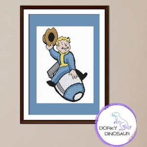 May include: Framed cross-stitch art featuring a cartoon character in a blue jumpsuit and a brown hat, riding a blue and white missile. The artwork is set against a white background with a blue border, in a brown frame.