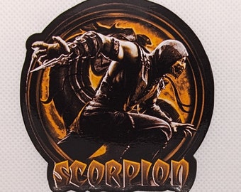 May include: A black and orange sticker featuring a character from Mortal Kombat. The character is in a fighting stance, with the word "SCORPION" in stylized text below. The sticker has a glossy finish.