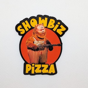 May include: A black and yellow sticker with a cartoon bear playing a guitar. The sticker says "Showbiz Pizza" in a yellow circle with a red background.
