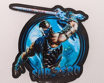 May include: A black and blue sticker featuring a character from the video game Mortal Kombat. The character is Sub-Zero, a ninja with a blue mask and a sword. The sticker has the text "Sub-Zero" in white letters.