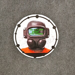 May include: A white circle with a black border and a black and brown astronaut helmet with a green screen that reads "You are a great asset to the company".