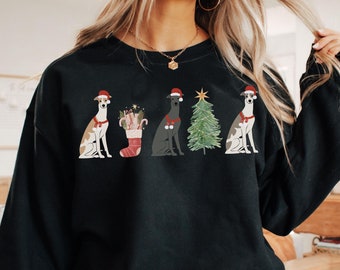 May include: Black sweatshirt with a Christmas-themed design. It features four greyhound dogs wearing Santa hats, a Christmas stocking, and a Christmas tree. The word "black" is printed at the bottom right.