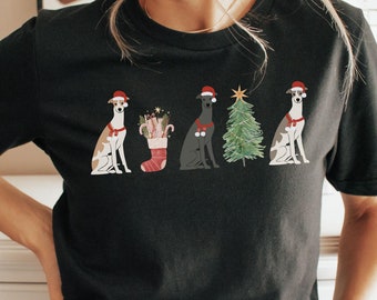 May include: Black t-shirt featuring a festive design with four dogs wearing Santa hats and holiday accessories. The dogs are depicted in various colors and poses, with a Christmas tree and stocking. The word "black" is printed at the bottom right.
