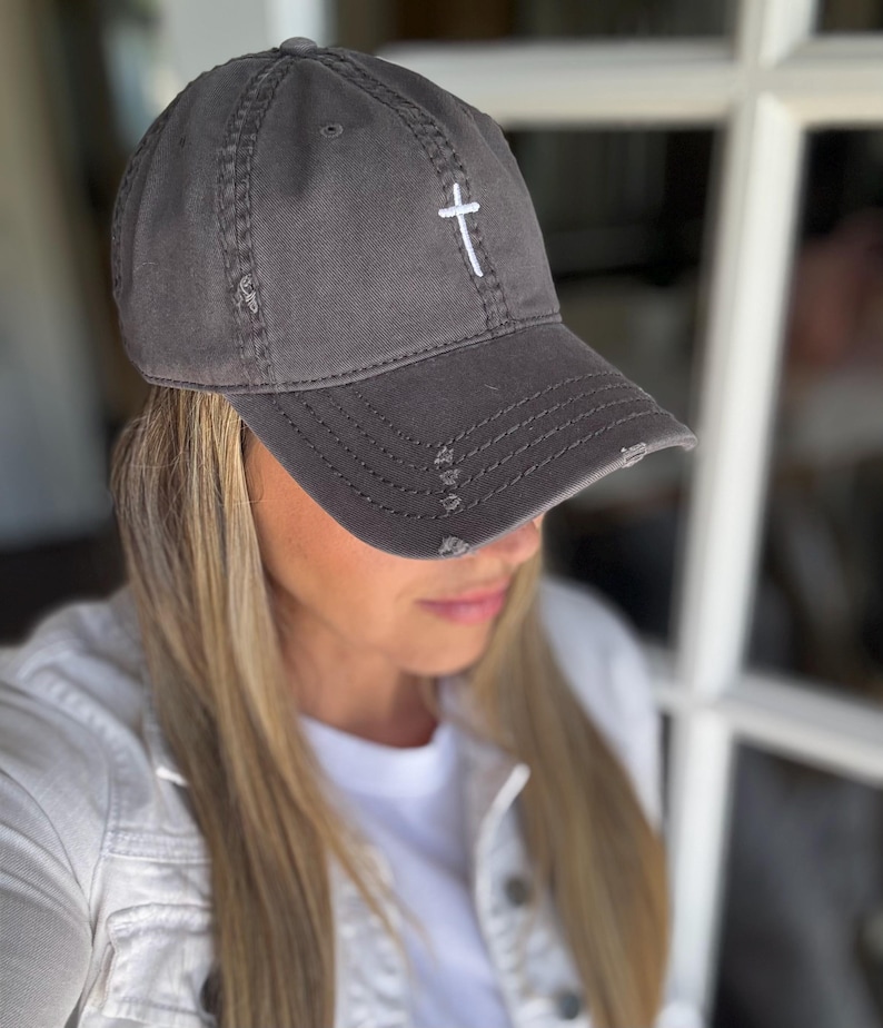 May include: A gray distressed baseball cap with a white embroidered cross on the front.