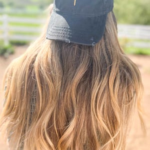 May include: A black distressed baseball cap with a gold cross embroidered on the front.