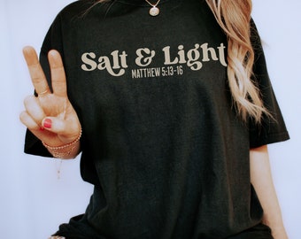 Könnte beinhalten: Schwarzes T-Shirt mit dem Text "Salt & Light" in einer Retro-Schriftart und dem Bibelvers "Matthäus 5:13-16" darunter.