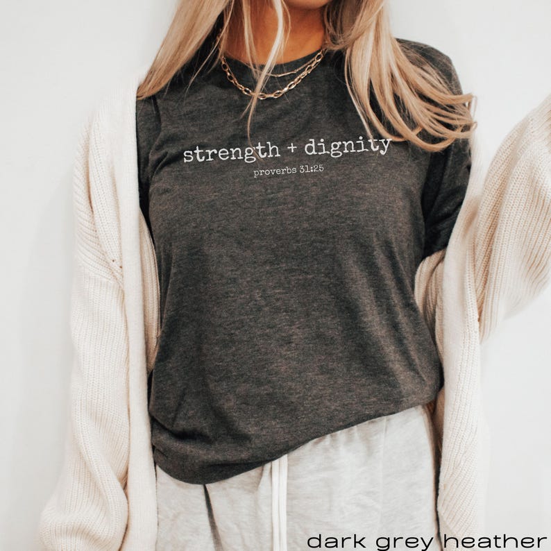 May include: A dark grey heather long-sleeve t-shirt with the text "strength + dignity" and "proverbs 31:25" printed in white.