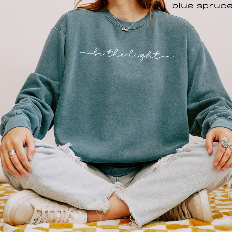 Pu&ograve; includere: Una felpa blu con il testo "be the light" in scrittura bianca sul davanti.