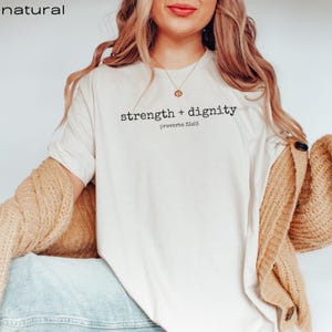 May include: White t-shirt with the text "strength + dignity" and "proverbs 31:25" printed on it.