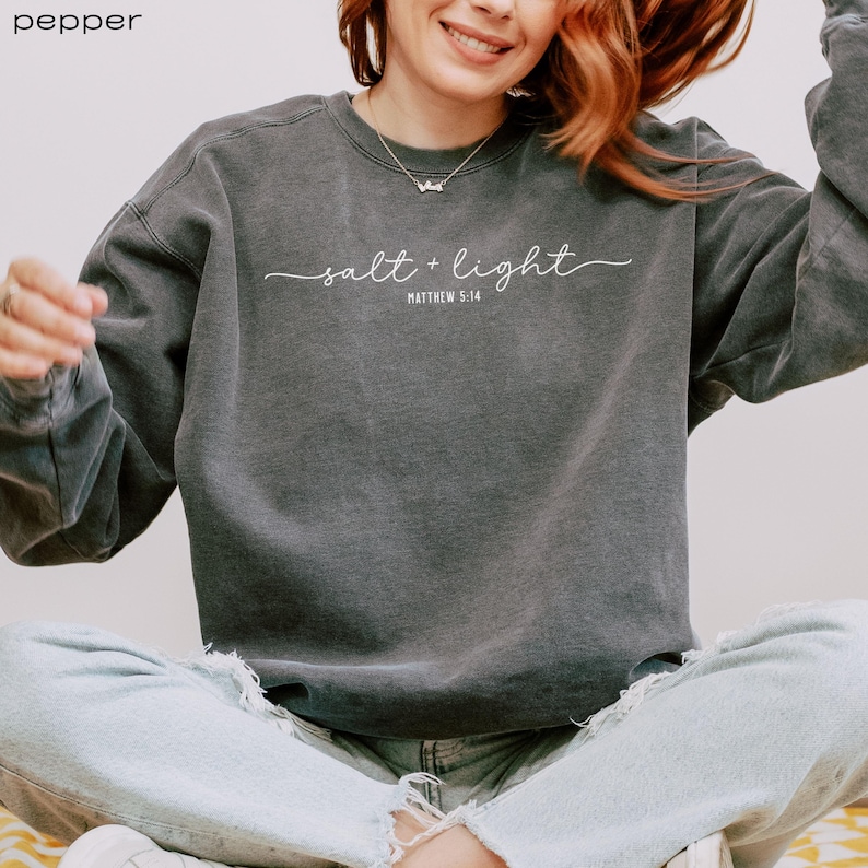 Puede incluir: Una sudadera gris antracita con el texto "salt + light" y "Matthew 5:14" en blanco.
