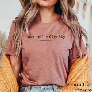 May include: A heather mauve t-shirt with the text "strength + dignity" and "proverbs 31:25" printed on the front.