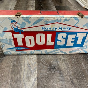 May include: A vintage metal toolbox with a red, white, and blue design. It features the words "Handy Andy Tool Set" and a cartoon character wearing a blue cap and overalls. The toolbox is labeled "Blue Diamond" and "A Product of Jet Craft Company, Chicago, U.S.A."