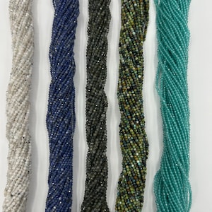 Puede incluir: Una variedad de hebras de cuentas en varios colores. Las hebras incluyen blanco, azul marino, gris oscuro, verde oliva y turquesa. Cada hebra está hecha de pequeñas cuentas redondas, fuertemente ensartadas. Las cuentas tienen un ligero brillo.