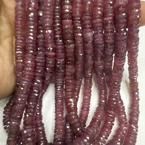 May include: Strands of faceted, deep red-purple gemstone beads. The beads are disc-shaped and strung together, creating a cascading effect. The gemstones have a polished, reflective surface, catching the light and displaying a range of color variations.
