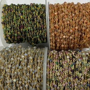 Puede incluir: Cuatro carretes de cadenas de cuentas de varios colores. Los carretes muestran cuentas verdes, naranjas, grises y multicolores ensartadas en alambre dorado. Las cuentas son pequeñas y facetadas, creando un efecto brillante. Las cadenas están enrolladas en carretes de plástico transparente.