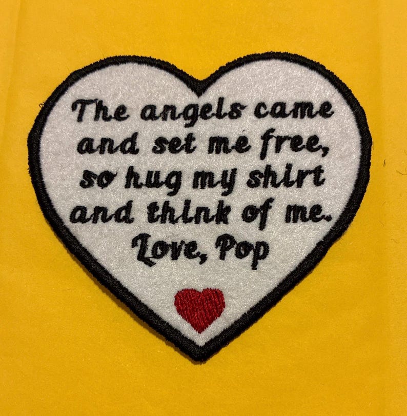 May include: Heart-shaped patch with black trim and the text "The angels came and set me free, so hug my shirt and think of me. Love, Pop." A small red heart is at the bottom. The background is yellow.