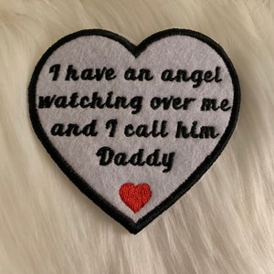 May include: White heart-shaped patch with black embroidered text that reads "I have an angel watching over me and I call him Daddy" with a small red heart at the bottom.