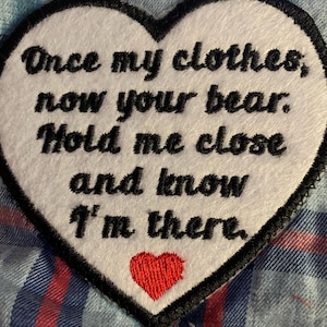 May include: White heart-shaped patch with black embroidered text that reads "Once my clothes, now your bear. Hold me close and know I'm there." A small red embroidered heart is at the bottom of the patch.