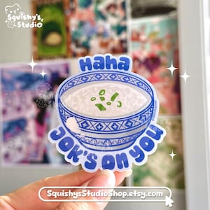 May include: A sticker featuring a bowl of congee with green onions, with the words "Haha" above the bowl and "Jok's on you" below. The sticker has a blue and white design and the text "SquishysStudioShop.etsy.com".