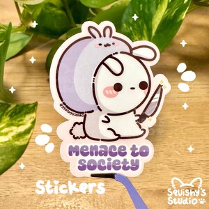 May include: A sticker featuring a cartoon bunny wearing a purple hooded cloak and holding a knife. The text "Menace to Society" is written below the bunny.