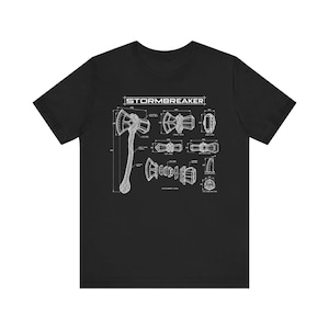 May include: A black short-sleeve t-shirt featuring a white technical blueprint graphic of the Stormbreaker axe. The design includes multiple views, an exploded view, and technical labels with measurements, showcasing the axe head and handle.