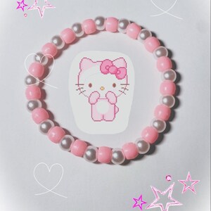 May include: Pink and white beaded bracelet with a Hello Kitty charm. The charm is a pixelated image of Hello Kitty wearing a pink bow.
