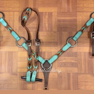 Puede incluir: Un conjunto de pechera y cabezada para caballos en turquesa, marrón y plata. El conjunto presenta detalles de cuero trenzado y herrajes plateados. El diseño incluye una pechera, una cabezada y correas de conexión.