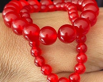 May include: A red beaded bracelet with two strands of round beads. The bracelet is made of smooth, polished stones.
