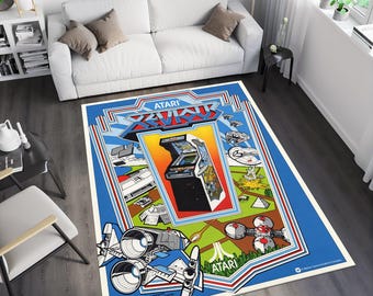 Puede incluir: Una alfombra azul y blanca con un diseño de videojuego retro. La alfombra presenta el logotipo de Atari y el texto "XEVIOUS". La alfombra también presenta una nave espacial y un gabinete de arcade de videojuegos.