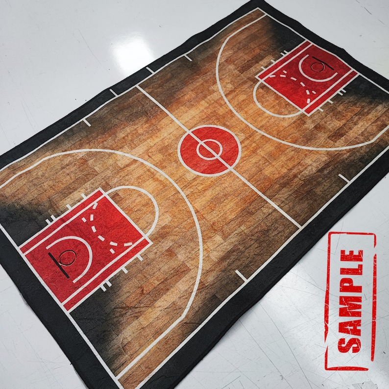 Peut inclure: Un tapis en tissu avec un motif de terrain de basket-ball noir et blanc. Le tapis pr&eacute;sente un motif de grain de bois brun et des lignes blanches marquant le terrain. Le tapis a une bordure noire.